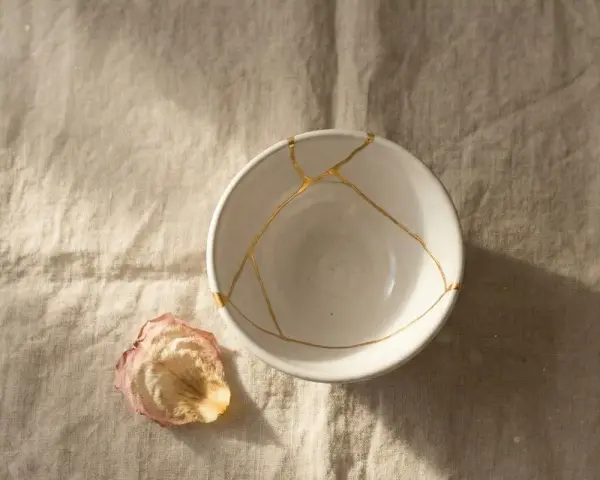 Biała miska z pęknięciami zespolonymi złotem, jak w kintsugi, obok zasuszonego płatka róży. Symbolizuje proces leczenia, jak w przypadku osobowości borderline test.
