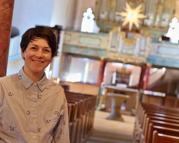 Eine lächelnde evangelische Pfarrerin steht in einer Kirche vor einer Orgel.