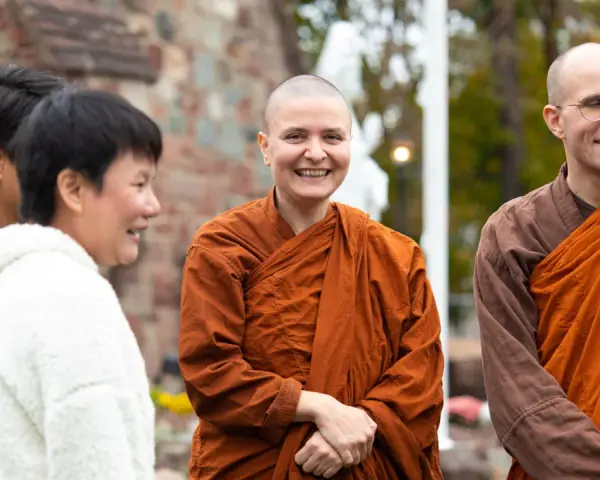 A smiling Buddhist monk in orange robes stands with others outside a church.