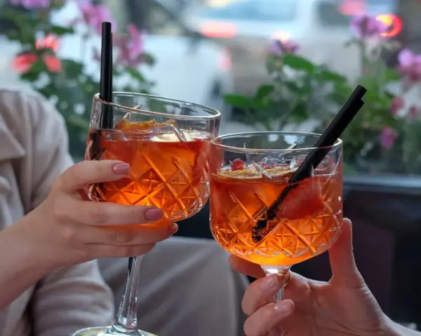 Dwie osoby wznoszą toast Aperolem. Orzeźwiający drink z pomarańczą i truskawką.