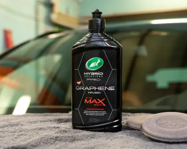 En flaska Turtle Wax Hybrid Solutions Pro Graphene Infused Wax, ett bilschampo för maximal glans och skydd, ligger på en grå handduk.