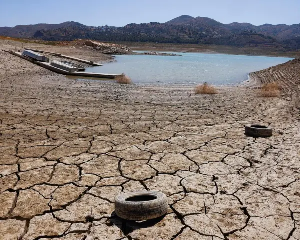 Seca tierra agrietada con un lago bajo y barcos varados. Neumáticos abandonados sugieren una contaminación natural y humana.