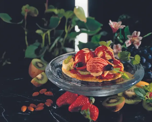 Eine süße Pizza mit Eis, Beeren und Kiwi. Mandeln und Trauben garnieren das Dessert.