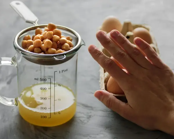 Kichererbsen im Sieb über Messbecher mit Aquafaba. Eier im Hintergrund. Perfekt für ei ersatz backen.