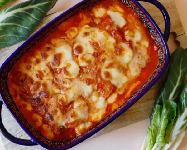 Piatto di verdure al forno con formaggio fuso, contornato da coste verdura fresche.