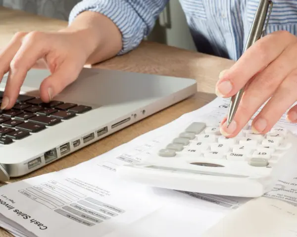 Main tenant calcule son solde de tout compte imposable sur une calculatrice, un ordinateur et des factures.