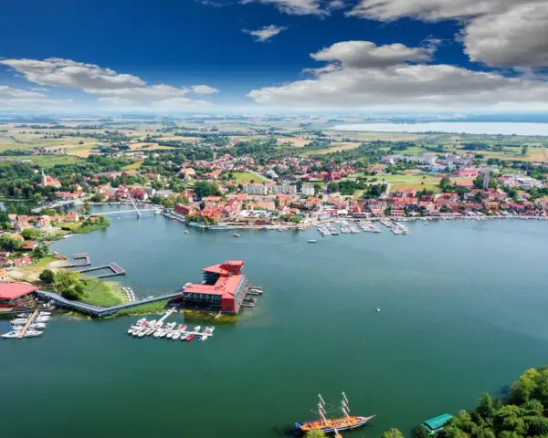 Malownicze miasta na Mazurach, które warto odwiedzić, rozciągają się wzdłuż jeziora. Widok na port z żaglówkami i zabytkową zabudowę.