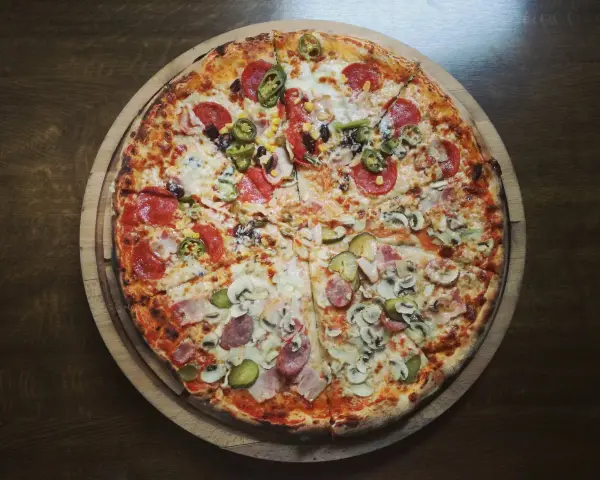 Cała pizza z różnymi dodatkami: salami, kukurydzą, papryczkami jalapeno, pieczarkami i ogórkiem.