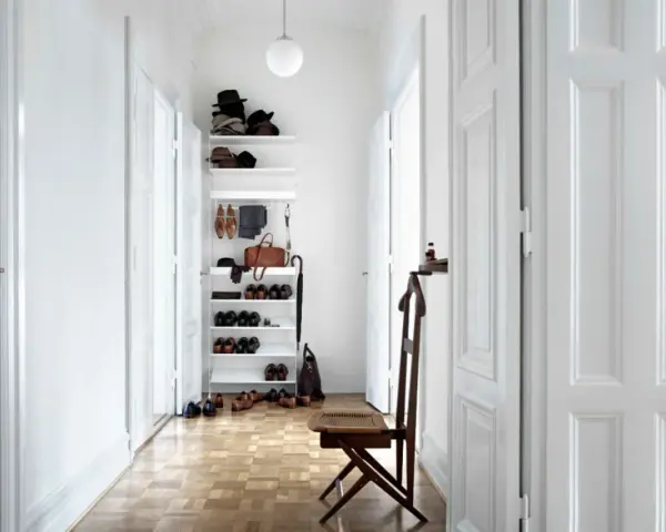Ein heller, schmaler Flur wirkt optisch breiter durch weiße Türen und eine offene Regalwand mit Schuhen und Accessoires.