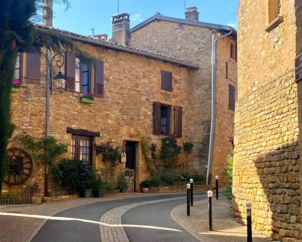 Village pittoresque aux maisons de pierre dorée, avec une ruelle sinueuse bordée de végétation luxuriante.