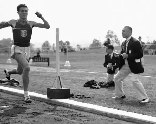 Louis Zamperini biegnie na bieżni, podczas gdy sędziowie obserwują zawody.