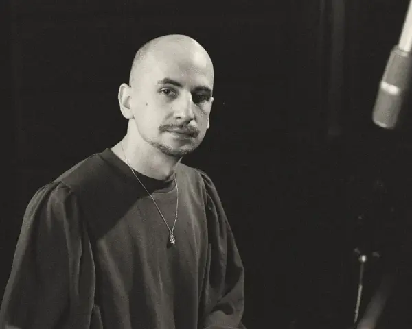Marek Pędziwiatr, z charakterystyczną łysą głową i wąsikiem, w ciemnej bluzie i z naszyjnikiem, przygotowuje się do nagrania.