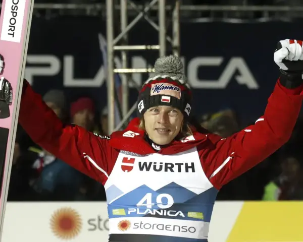 Skoczek narciarski w czerwonej kurtce i czapce z polską flagą świętuje zwycięstwo na skoczni. Mistrzostwa świata w skokach narciarskich.