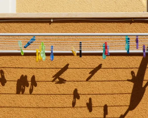 Variados tipos de tendederos exteriores con pinzas de colores sujetan la ropa. Las sombras proyectadas crean un patrón interesante sobre la pared texturizada.