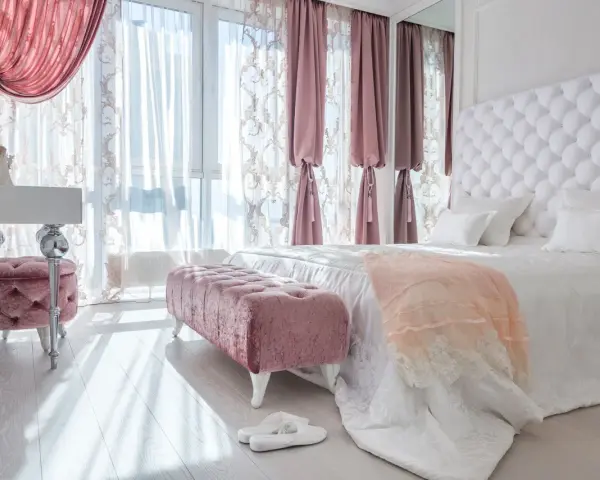 Elegancka sypialnia w stylu angielskim z pikowanym zagłówkiem, różowymi pufami i zasłonami.