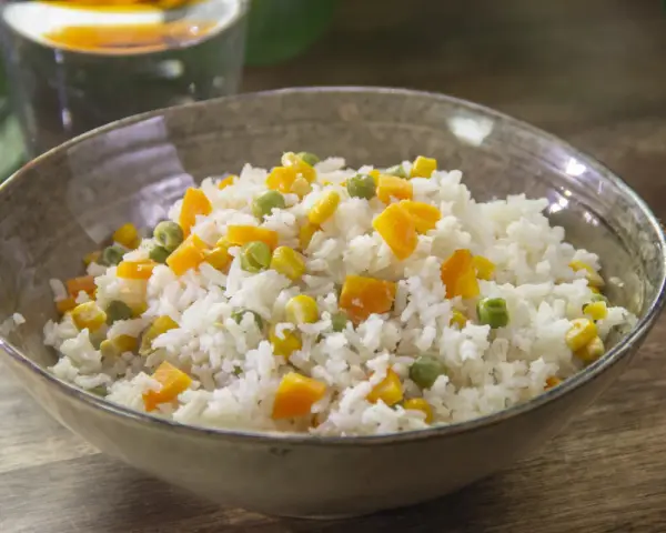 Un tazón de arroz blanco con trozos de zanahoria, guisantes y maíz. Un plato sencillo y colorido de arroz con verduras.