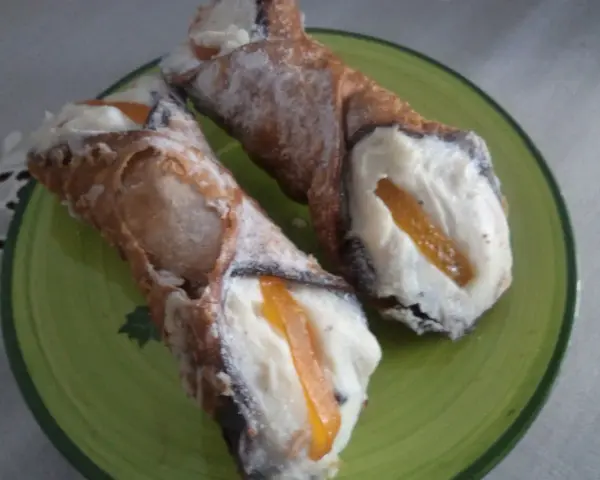 Dwa pyszne cannoli z kremem i kandyzowaną skórką pomarańczową, posypane cukrem pudrem. Ten makaron to prawdziwa rozkosz!