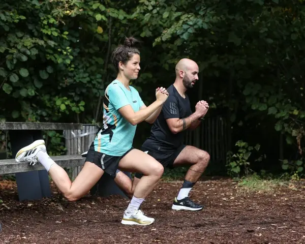 Un couple fait des exercices de renfo course à pied en extérieur, avec des fentes et des squats.