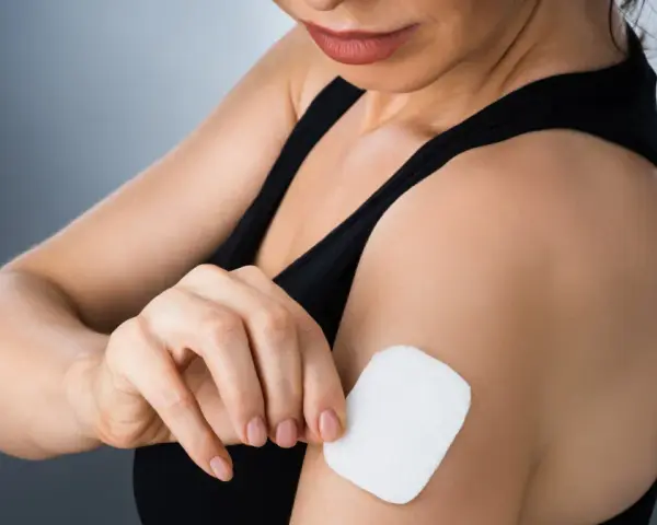 Kobieta przykleja plaster antykoncepcyjny na ramię. Dyskretny sposób na kontrolę płodności.