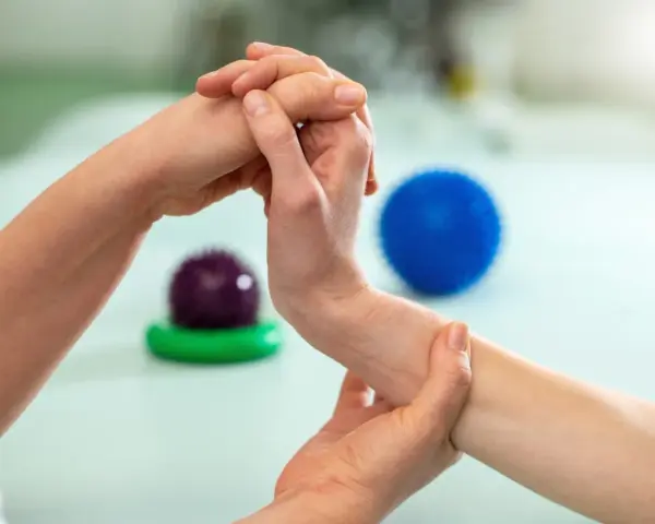 Fizjoterapeuta pomaga pacjentowi w ćwiczeniach na palec trzaskający, używając masażu i piłeczek do rehabilitacji.