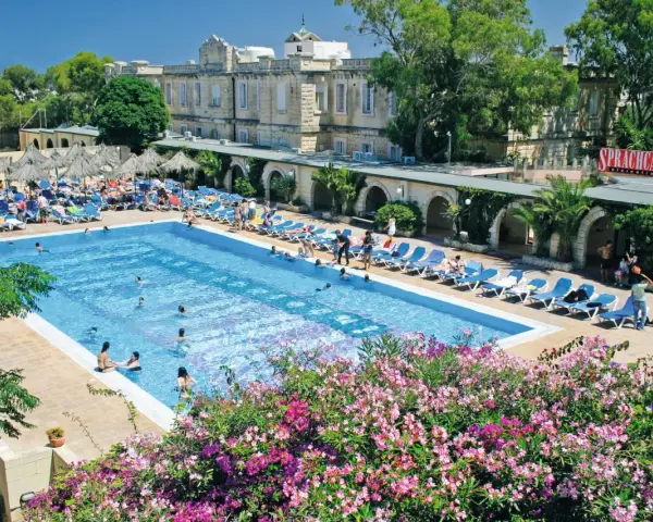 Profitez de vos vacances scolaires à Malte au bord de cette piscine animée, entourée de transats et de végétation luxuriante.