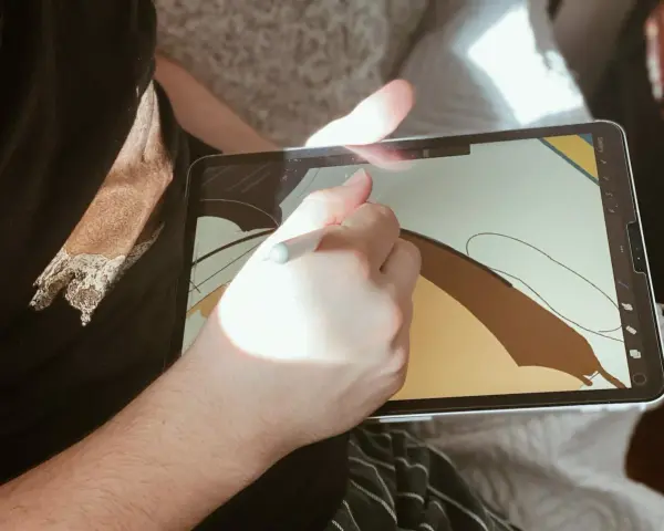 Osoba rysuje na ekranie iPad'a, używając rysika. To cyfrowy tablet graficzny, idealny do tworzenia sztuki.