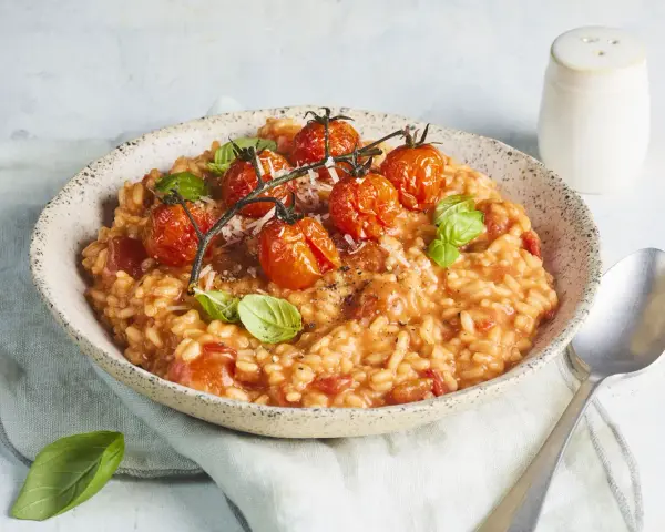 Cremiges Tomaten Risotto, garniert mit frischen Basilikumblättern und gerösteten Kirschtomaten. Ein Genuss für jeden Liebhaber italienischer Küche.