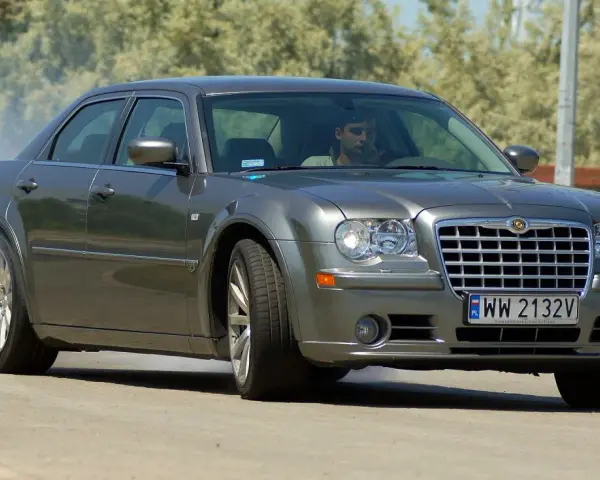 Szary Chrysler 300S z dymiącymi oponami, kierowca za kierownicą, na drodze.