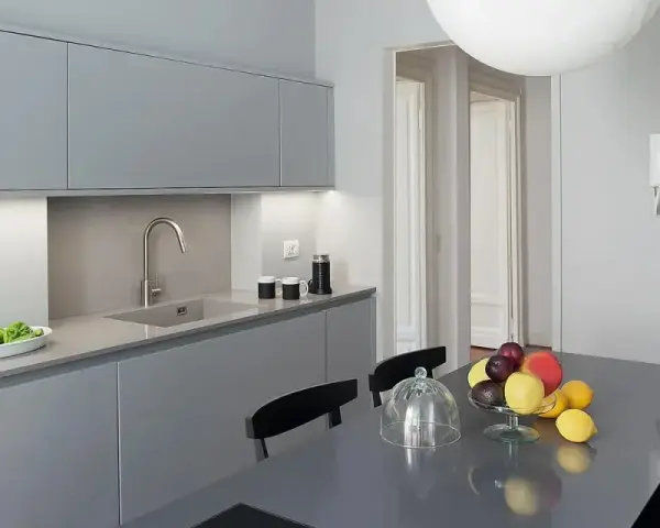 Cucina moderna con pensili e basi grigie. Il colore pareti neutro esalta la pulizia delle linee. Tavolo con frutta fresca.
