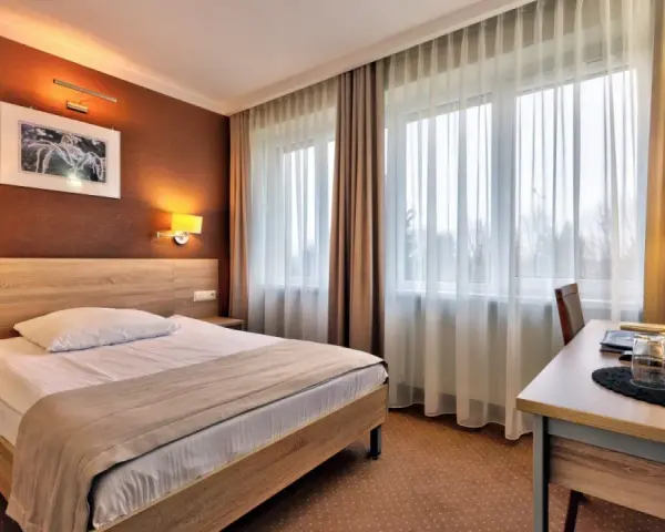 Przytulny pokój hotelowy w Białymstoku z wygodnym łóżkiem, biurkiem i telewizorem.