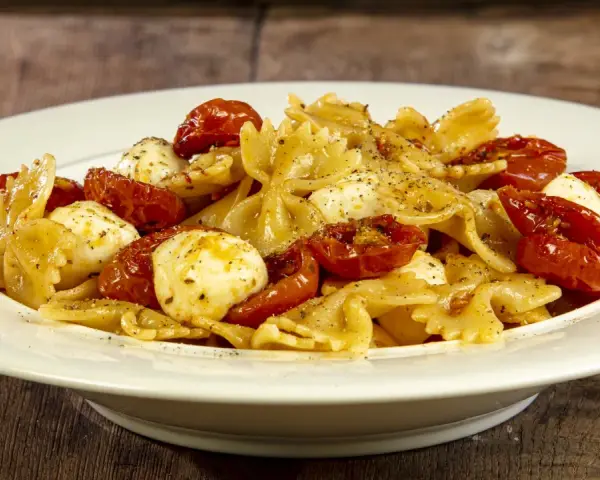 Farfalle con pomodorini confit, mozzarelline e un tocco di acciughe. Un piatto semplice e gustoso.