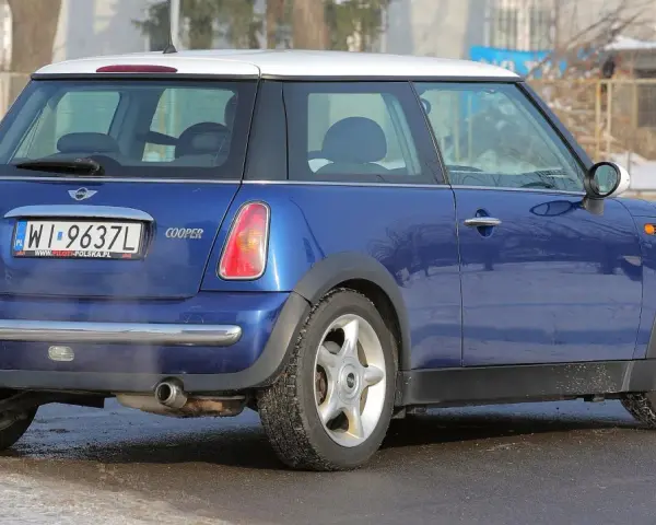 Niebieski Mini Cooper R50 z białym dachem, zaparkowany na zaśnieżonej drodze.
