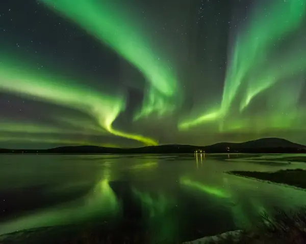 Grönt norrsken dansar över en frusen sjö i Finland. Stjärnor lyser på himlen och speglar sig i vattnet.