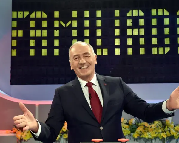 Uśmiechnięty prowadzący w garniturze na tle planszy z zielonymi polami, jak w Familiadzie. Ile lat ma ten program?