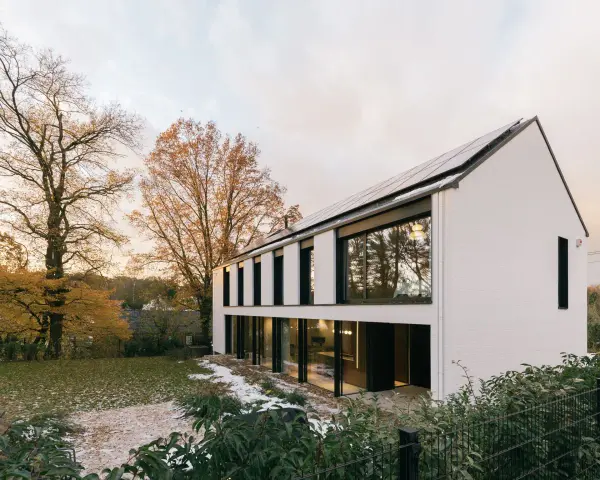 Agrandissement maison ossature bois moderne avec panneaux solaires, entourée d'arbres aux couleurs d'automne et d'un jardin enneigé.