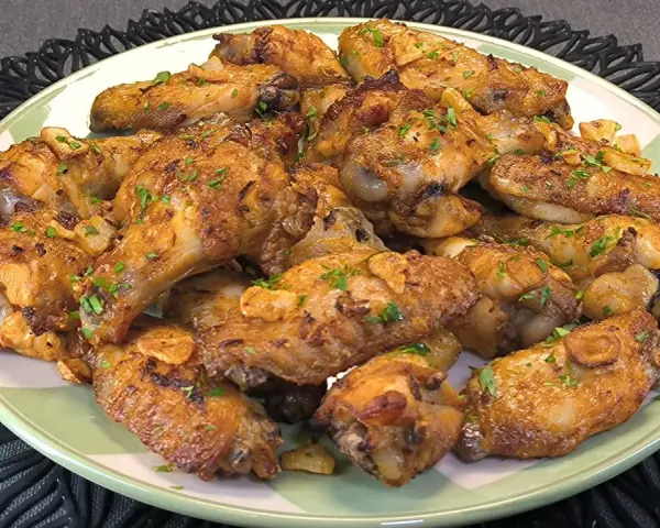 Alitas de pollo doradas con ajo y perejil en un plato verde.