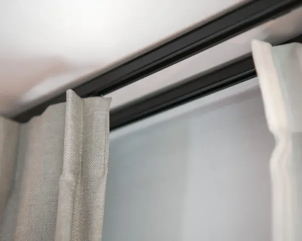 Ciemna szyna sufitowa z zasłonami w jasnych kolorach.