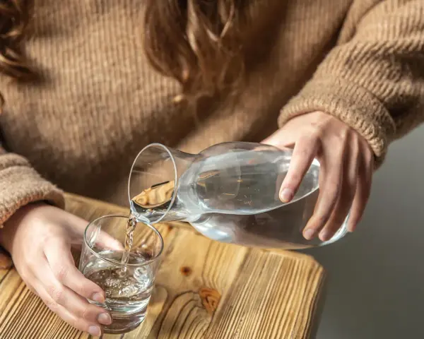 Dłonie nalewają wodę z karafki do szklanki. Pamiętaj, by stay hydrated.