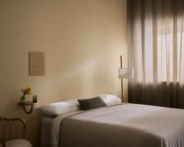 Ett lugnt sovrum med beige väggar, en bekväm säng och en golvlampa. Perfekt för att måla sovrum i en avkopplande stil.