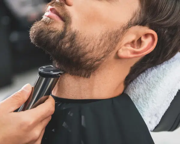 Barbero perfilando barba con recortadora, creando diseños de barba modernos.