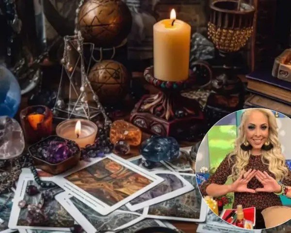 Mesa esotérica con cartas, cristales y velas. Una mujer sonríe haciendo un gesto con las manos, quizás buscando cómo atraer el amor.