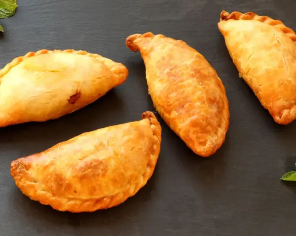Cuatro empanadillas doradas y crujientes dispuestas sobre una superficie oscura, con hojas de menta a los lados.