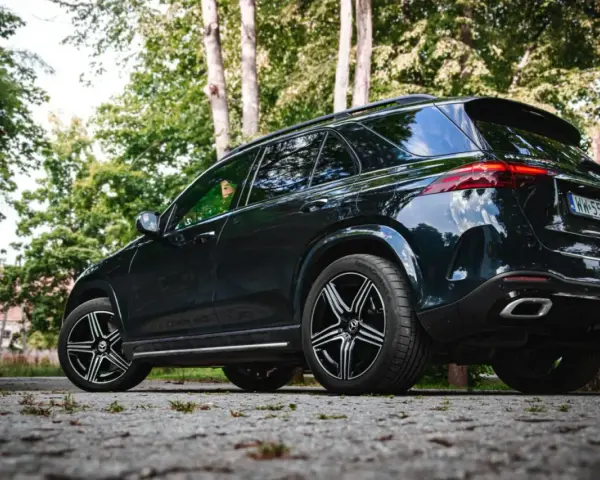 Ciemny Mercedes GLE 350 zaparkowany na kamienistej drodze, otoczony zielenią drzew.