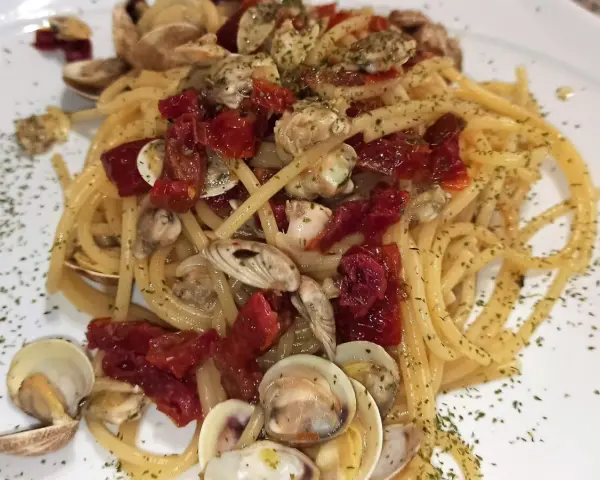 Spaghetti con lupini e pomodorini secchi, un piatto di mare saporito e profumato, guarnito con prezzemolo tritato.