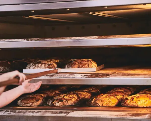 Bäcker lässt den **backofen spalt offen lassen beim backen** für knuspriges Brot. Mehrere Brote auf Regalen im Ofen.