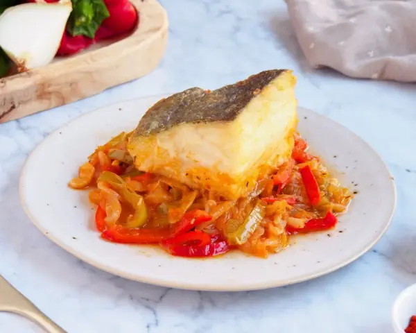 Un delicioso bacalao encebollado reposa sobre una cama de pimientos y cebolla.