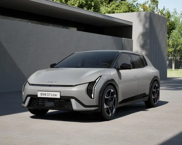 Nowoczesny, jasnoszary Kia EV4 GT-Line stoi na podjeździe przed minimalistycznym budynkiem.