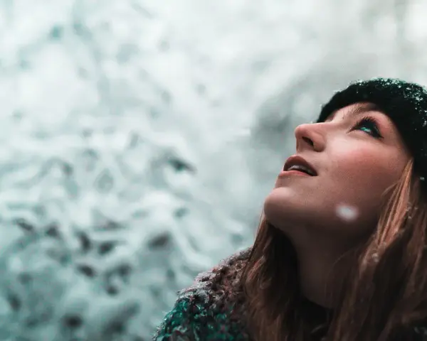 Junge Frau blickt in den Schnee, ihre Wangen gerötet, ein Zeichen von trockene Haut im Winter.