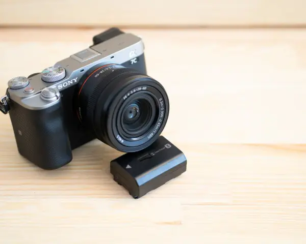 Srebrno-czarny aparat Sony a7c z obiektywem i zapasową baterią na drewnianym tle.