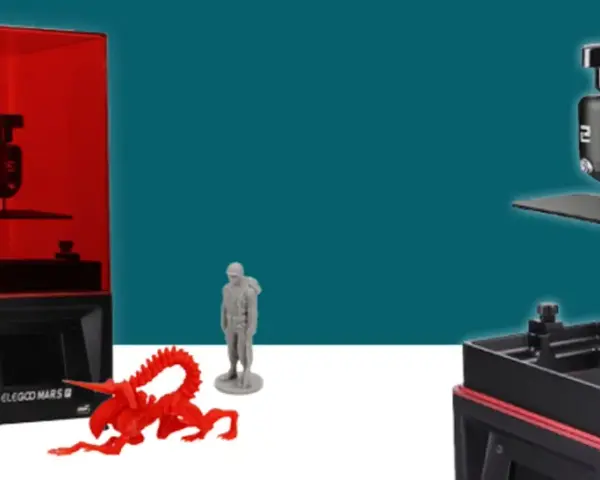 Dwie drukarki 3D, jedna z czerwonym filtrem UV, obok wydrukowanych figurek: stworka, żołnierza i kosmity. To modele z serii Mars 2.